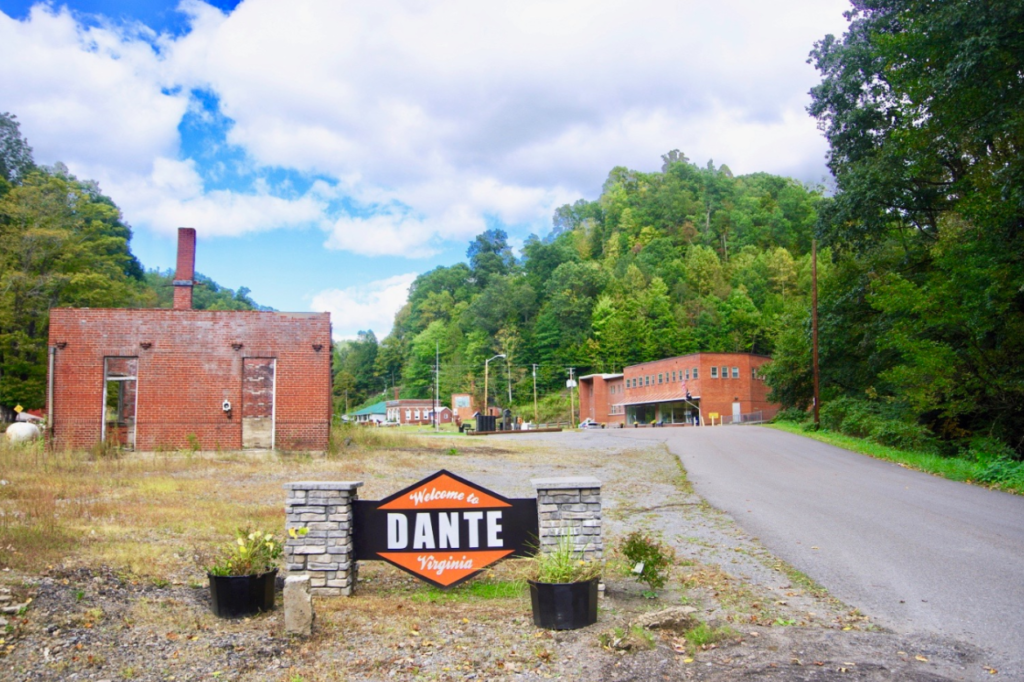 This image shows abandoned mine land. There is an old road leading up to abandoned brick structures. There is a sign in the foreground. It reads: Dante.