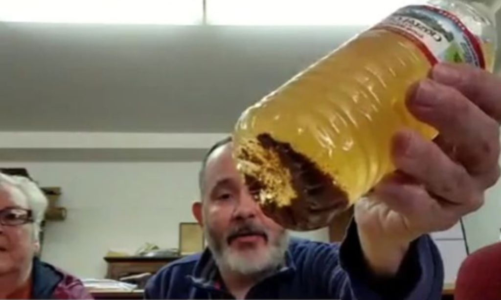 Image show's Reverand Brad Davis holding up a bottle of brown water that was collected from a resident of Leckie West Virginia's bathroom sink as he discusses the ongoing water crisis.